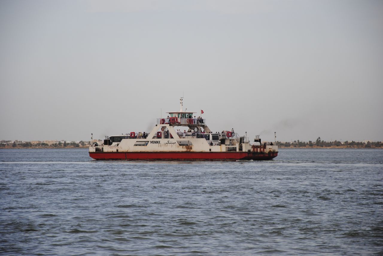 A ferry transports passengers across the ocean in Jorf, Tunisia, with a distant coastline in view.