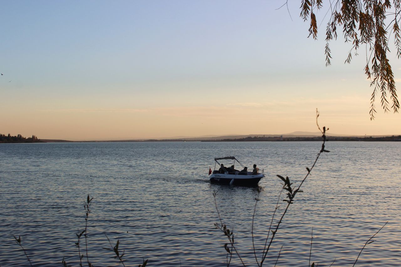 Motorboat on a serene lake at sunset with scenic views and silhouette of people.