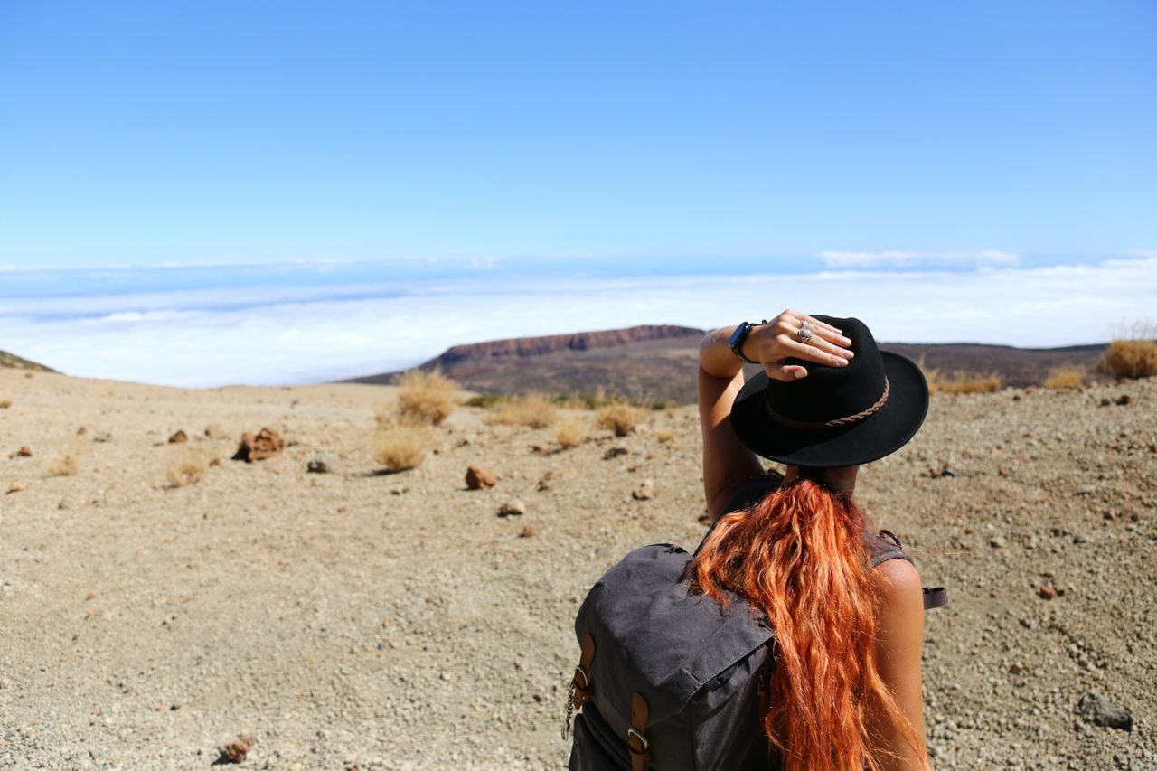 About Woman standing in a desert landscape, looking at distant mountains, wearing a hat and backpack.