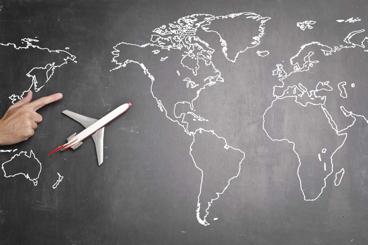 who-we-are Top view of miniature airplane placed on over gray world map with crop hand of anonymous person indicating direction representing travel concept