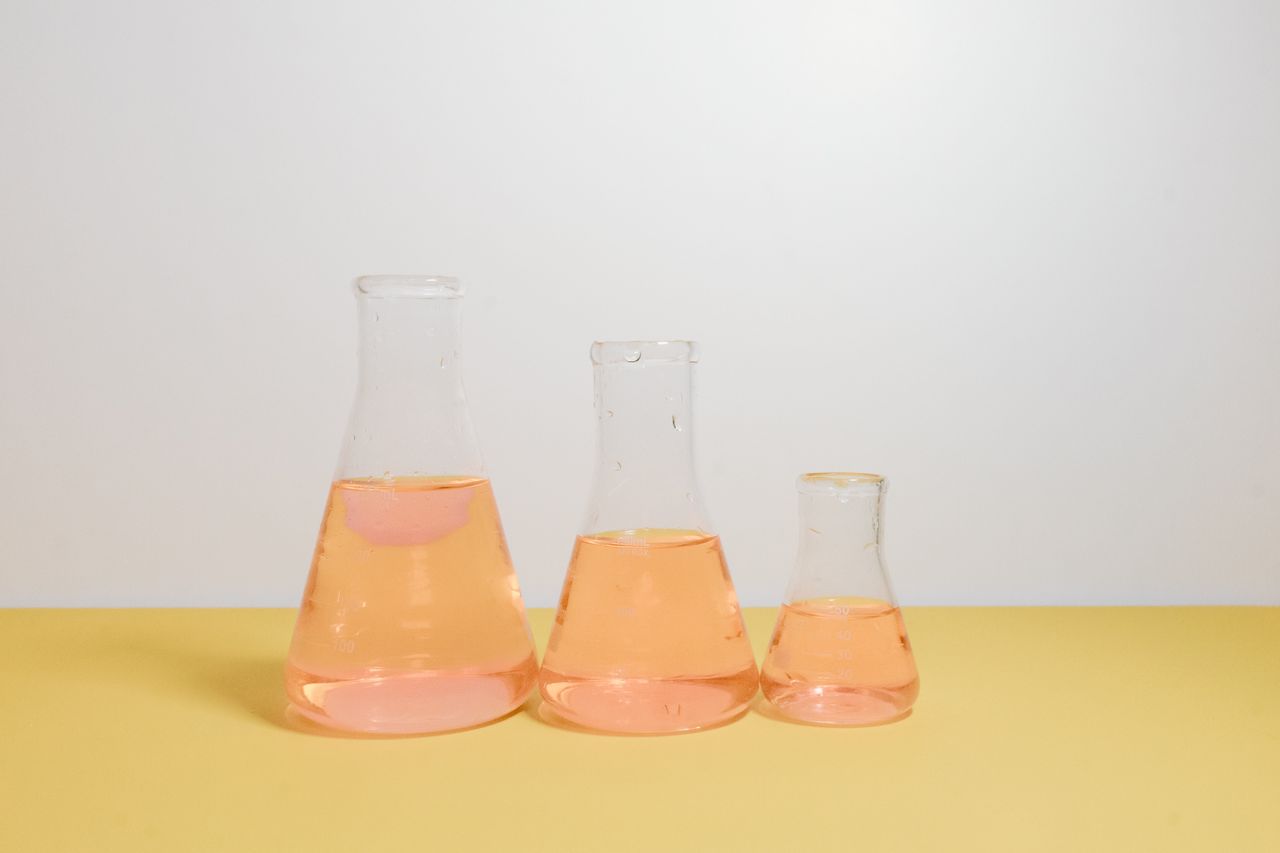team-03 Three Erlenmeyer flasks filled with pink liquid on a yellow surface in a lab setting.