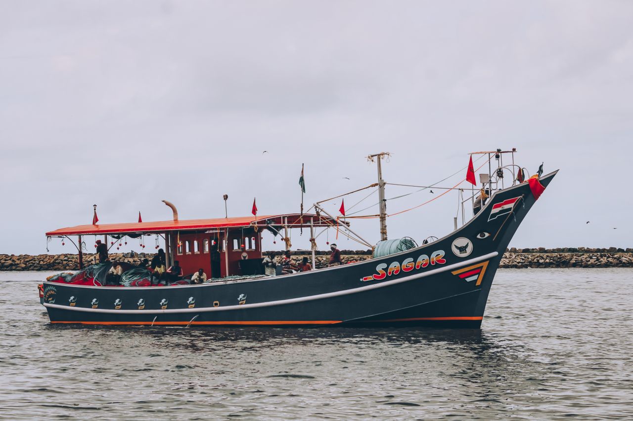 A beautiful Indian fishing boat with colorful flags sails on a cloudy day, showcasing maritime culture.